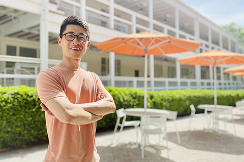 Assistant Professor Haoluan Wang looks at the camera, smiling with his arms crossed. The white Campo Sano building is behind him.  
